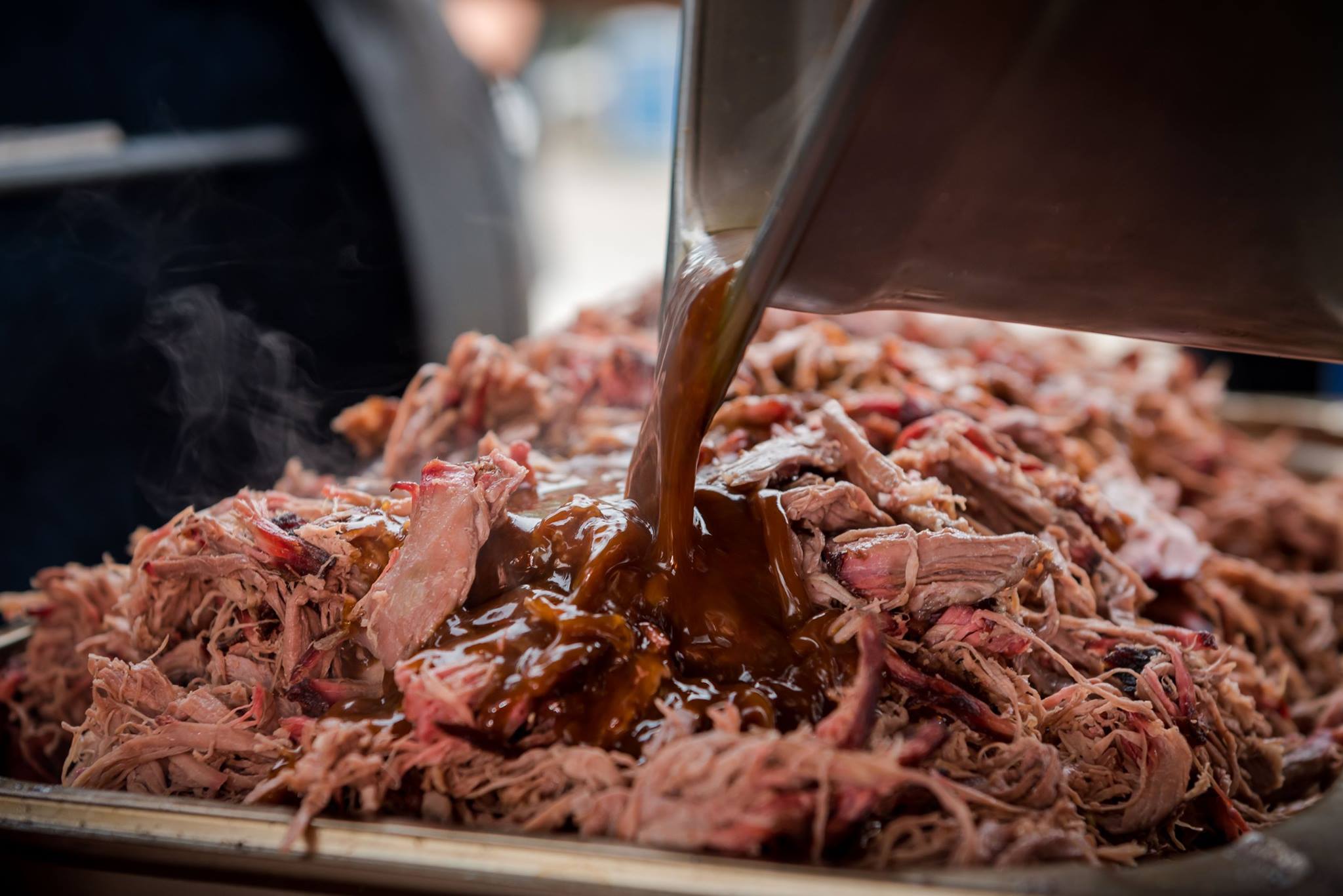 Frisch gezupftes Pulled Pork wird mit BBQ-Sauce übergossen, Dampf steigt auf